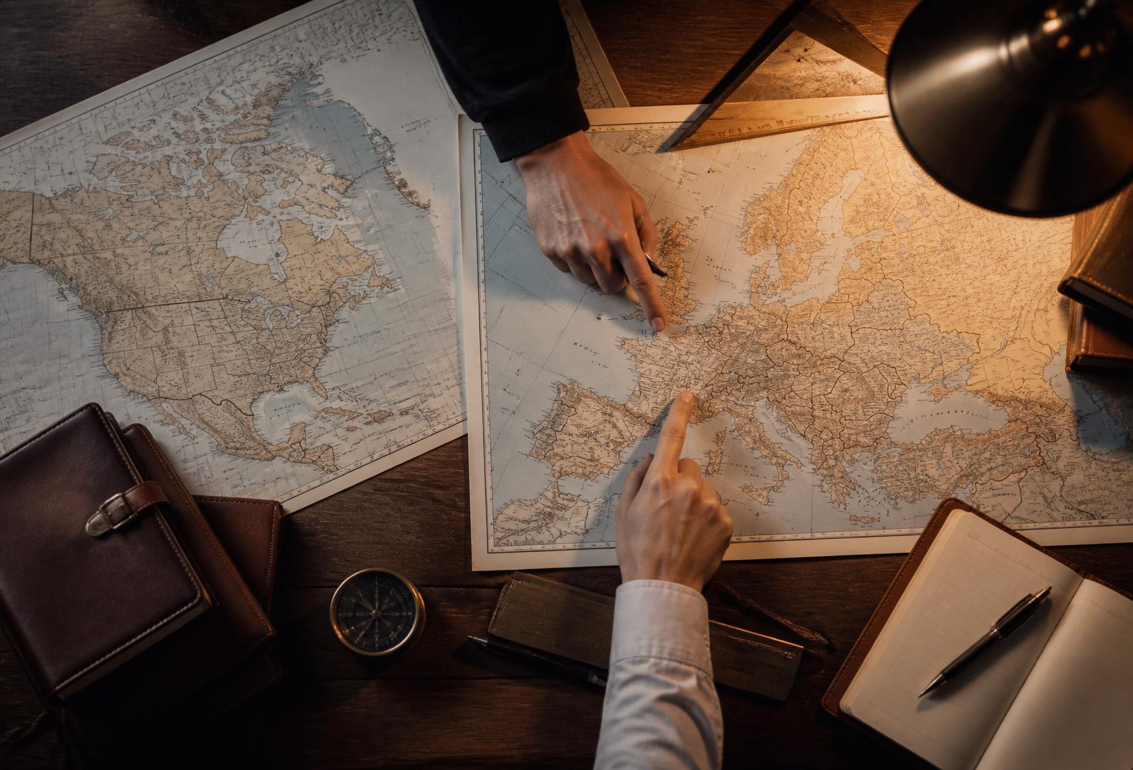 Overhead view of paper maps of Europe and North America on a wooden desk with hands pointing at locations, evoking strategic planning.