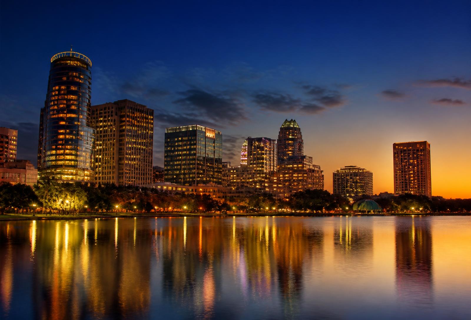 Downtown Orlando, Florida skyline at dusk reflected on the lake, warm sunset sky.
